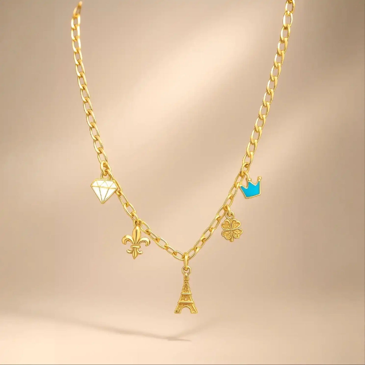 A gold chain necklace adorned with five charms: a white diamond, a gold fleur-de-lis, a gold Eiffel Tower, a gold four-leaf clover, and a blue crown.