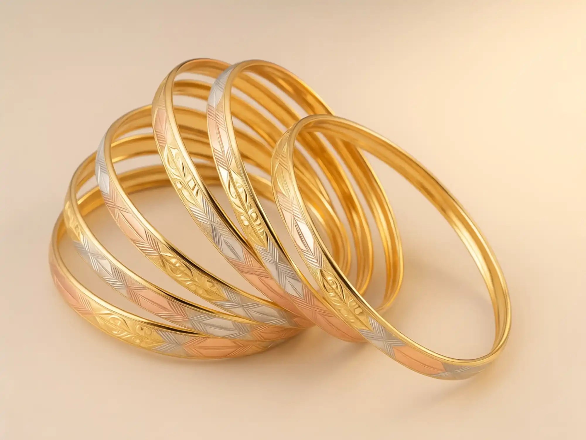 A stack of gold bangles with engraved patterns, some in multi-tone gold.